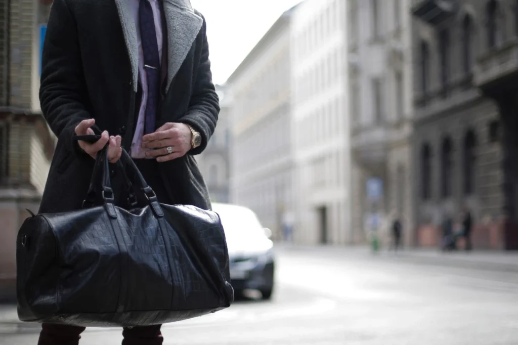 Person carrying a large travel bag while walking through a busy city, illustrating a grab-and-go bag for a full day out