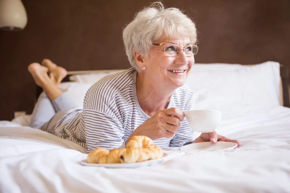 Smiling older woman enjoying coffee and breakfast in bed