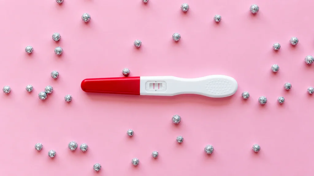 Positive pregnancy test with two lines on a pink background decorated with silver spheres